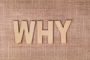 Wooden letters spelling 'WHY' on a textured burlap fabric, inviting curiosity and reflection.