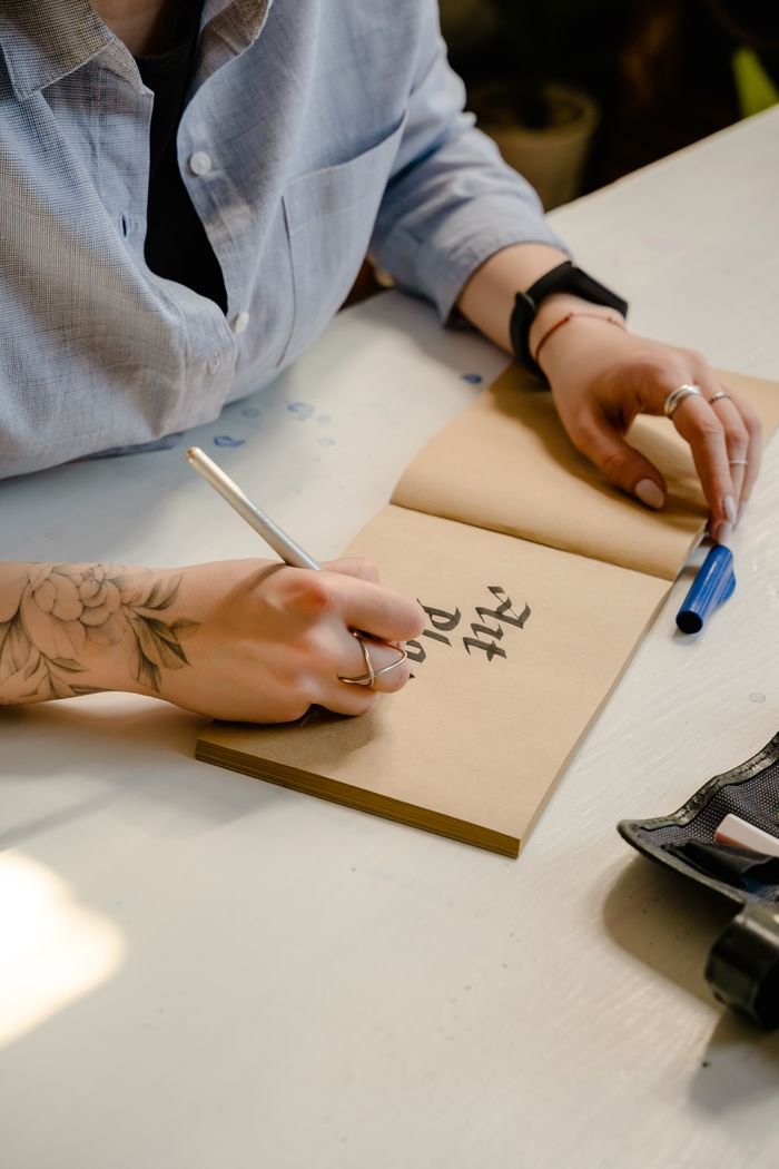 Person practicing artistic calligraphy on brown paper indoors.